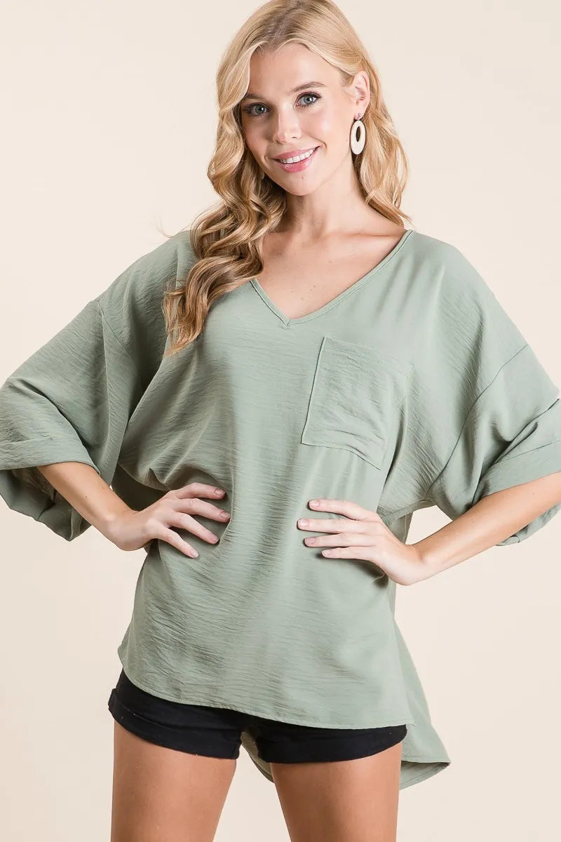 Sage green BiBi Flowy Woven V-Neck Top with rolled-up cuffs, stylish and lightweight for a casual, feminine look.