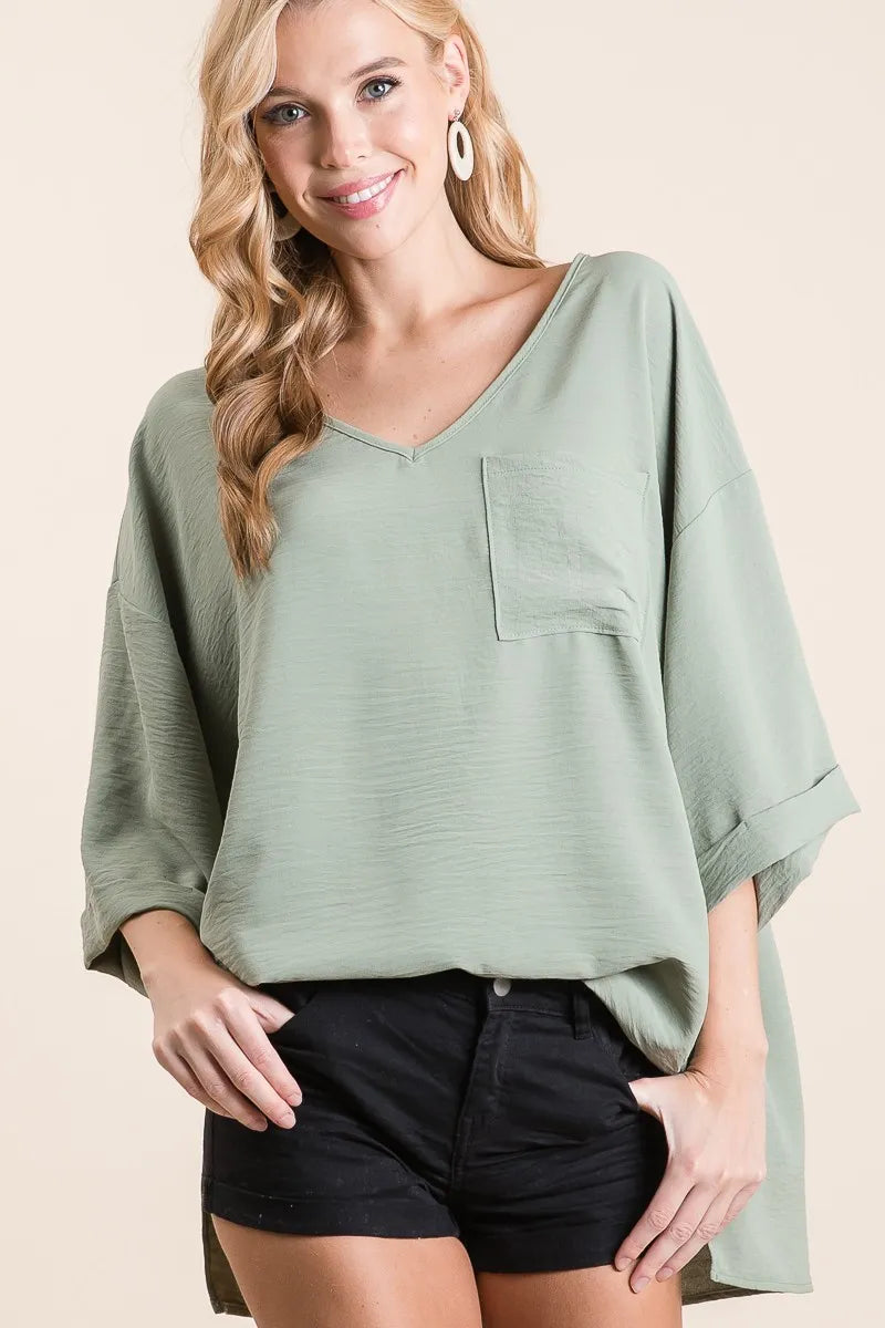 Sage green BiBi Flowy Woven V-Neck Top with rolled-up cuffs, stylish and lightweight for casual wear.