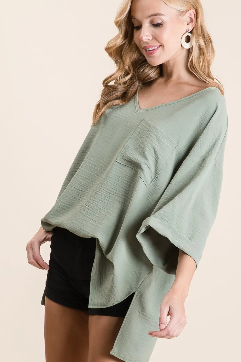 Sage green BiBi Flowy Woven V-Neck Top by Trendsi with rolled-up cuffs and relaxed fit, displayed on a hanger.