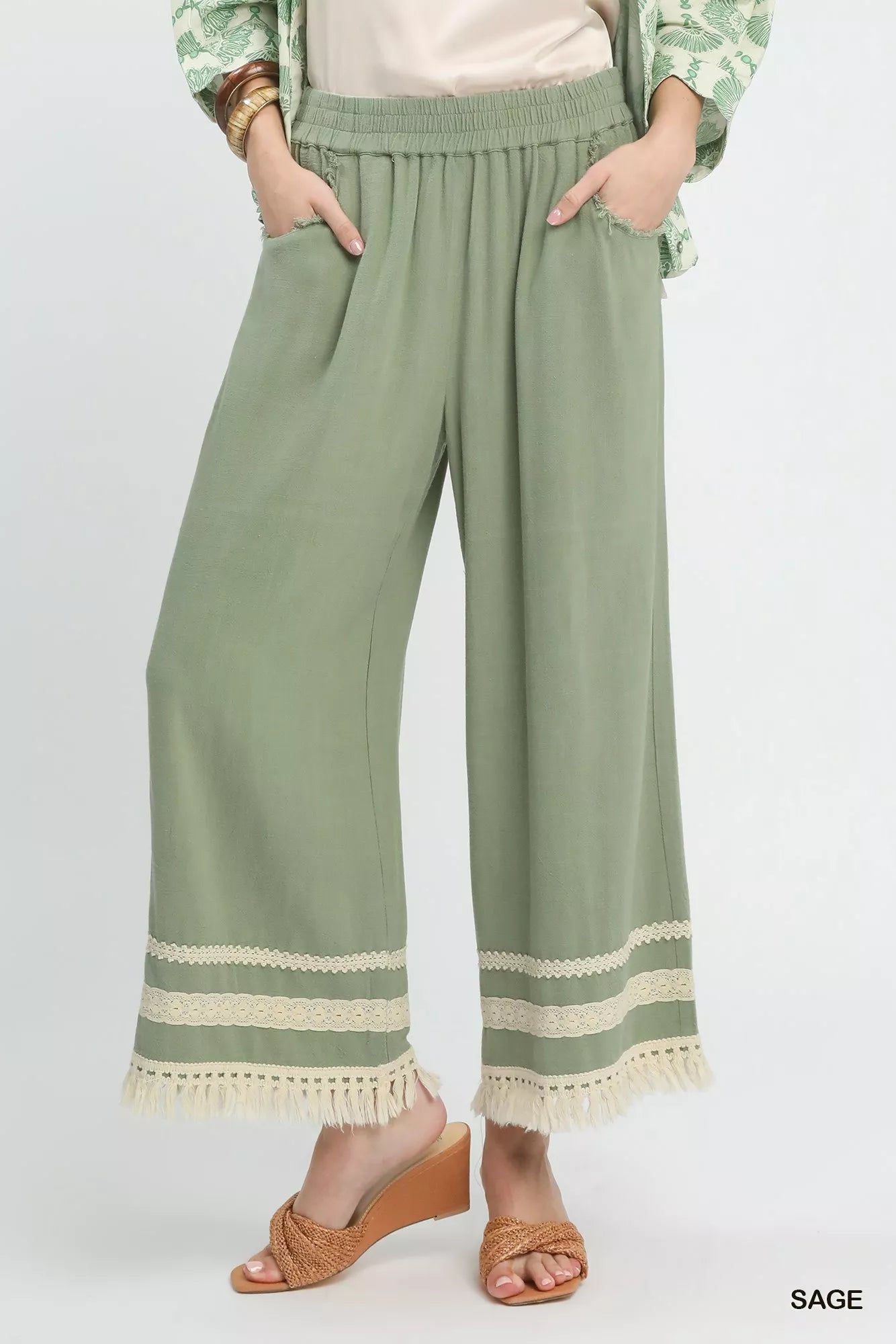 Sage green Umgee wide leg pants with lace trim and fringe hem, featuring a relaxed fit and stylish design.