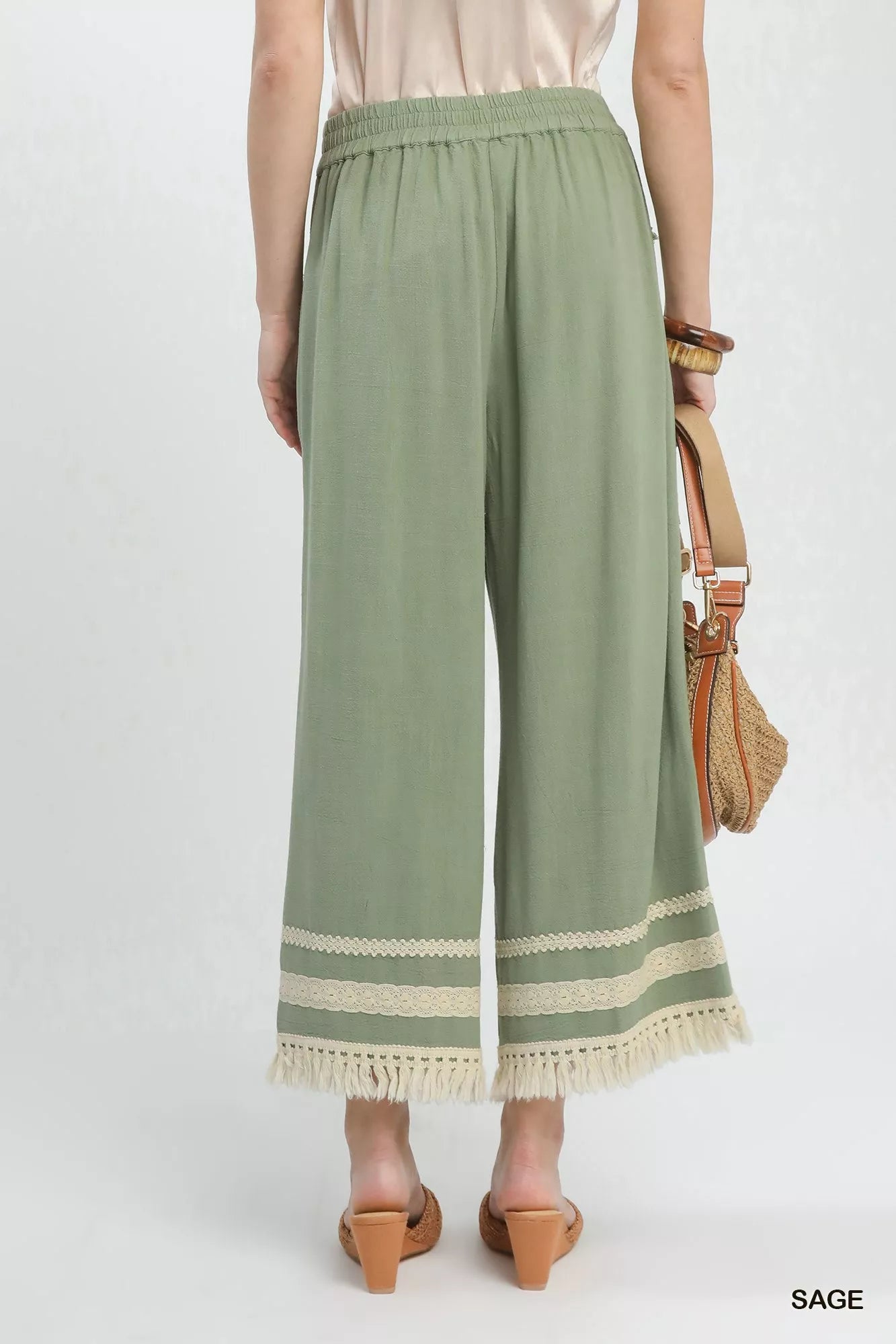 Sage green Umgee lace trim fringe hem wide-leg pants from Trendsi, showing the flowy fabric and detailed hem design.
