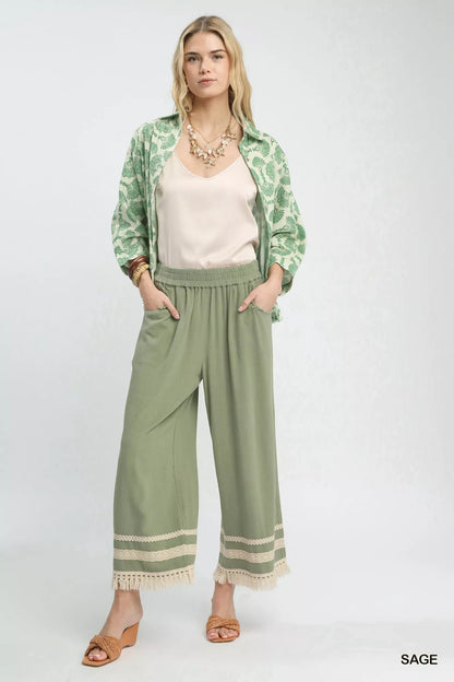 Sage green Umgee wide leg pants with lace trim and fringe hem, featuring a relaxed fit and stylish design.